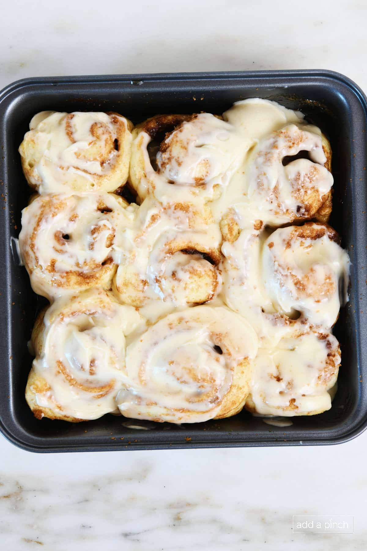 Pan of freshly baked pizza dough cinnamon rolls that have cream cheese frosting spread on them.