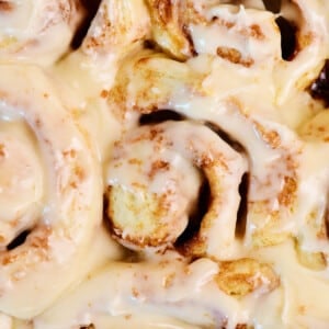 Cream cheese frosting covered cinnamon rolls in a pan.