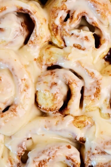 Cream cheese frosting covered cinnamon rolls in a pan.