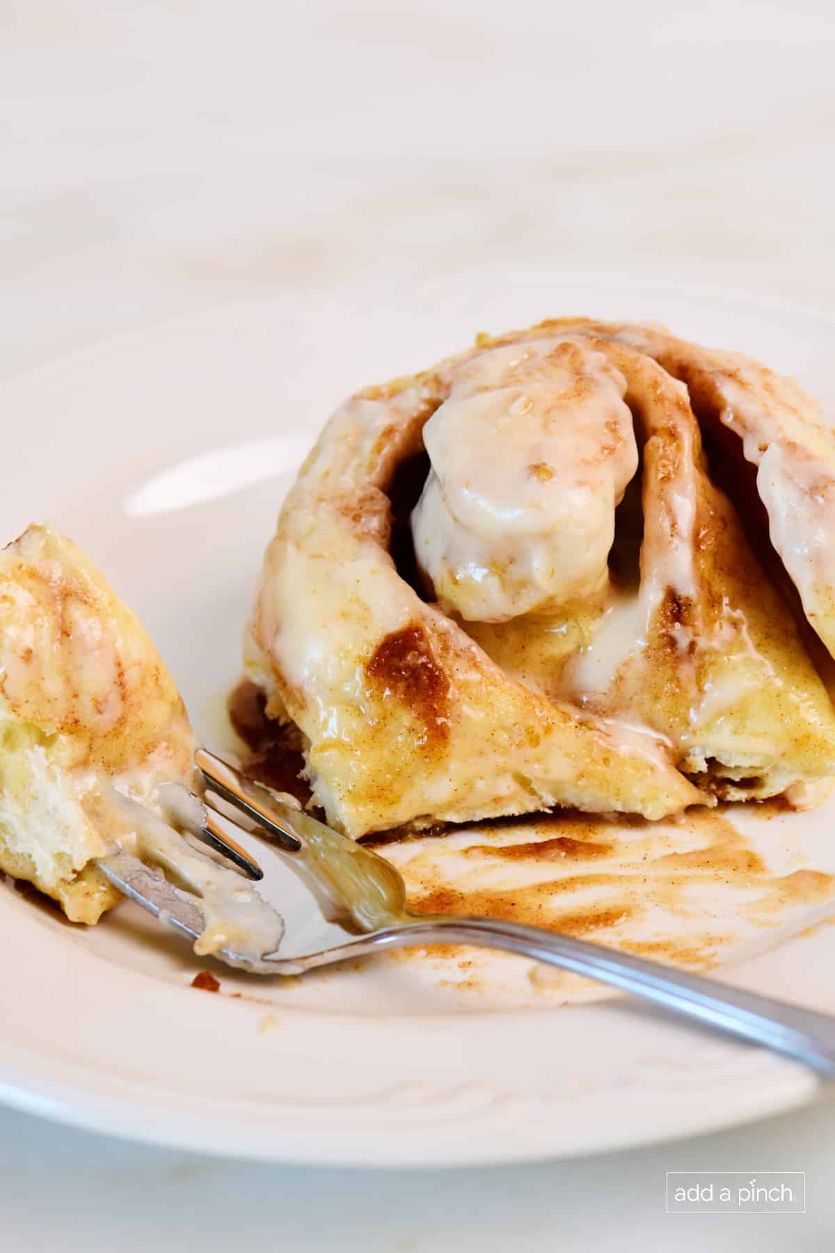 Pizza dough cinnamon roll is served on a white plate with a fork.