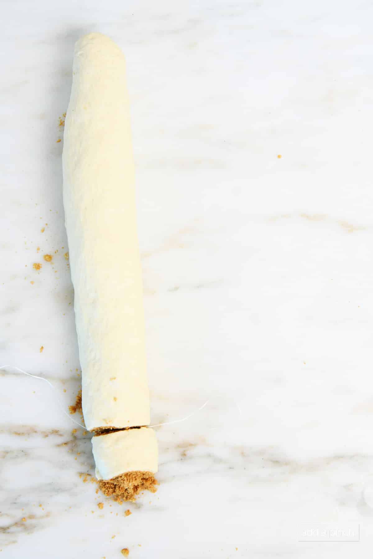 Log of cinnamon roll dough is sliced, showing cinnamon filling inside.