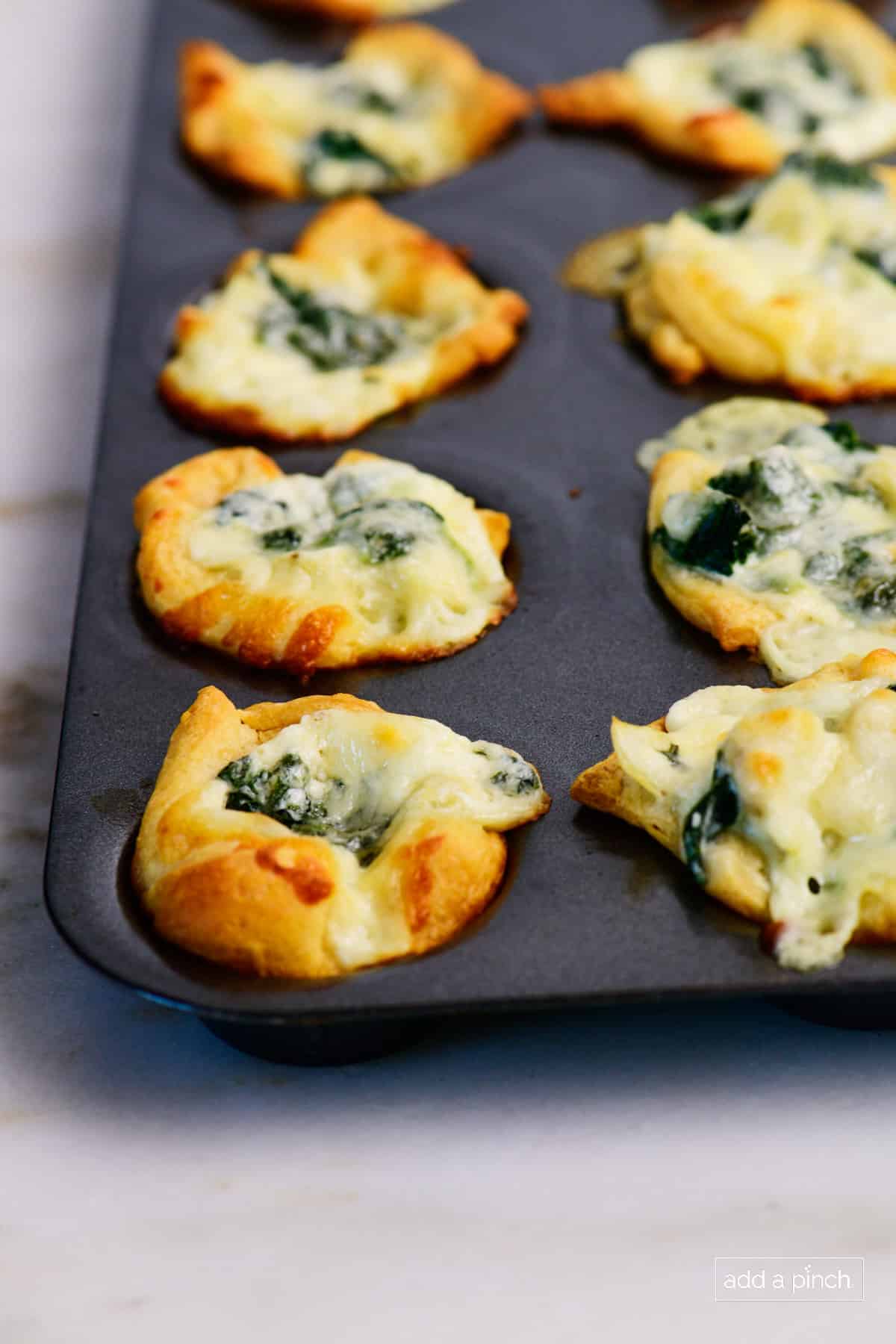 Golden brown baked spinach dip bites in a muffin tin.