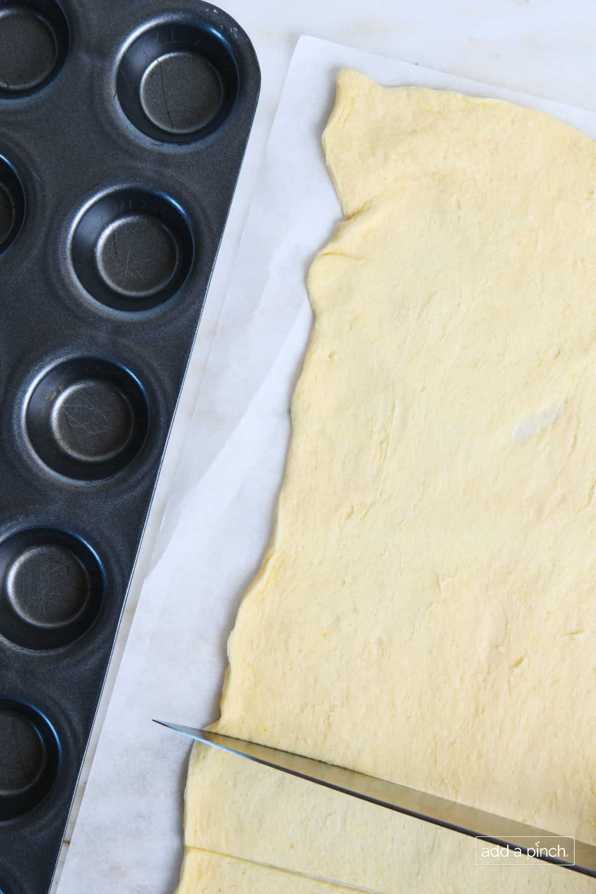 Mini Muffin tin lies beside a crescent dough roll being cut into squares.