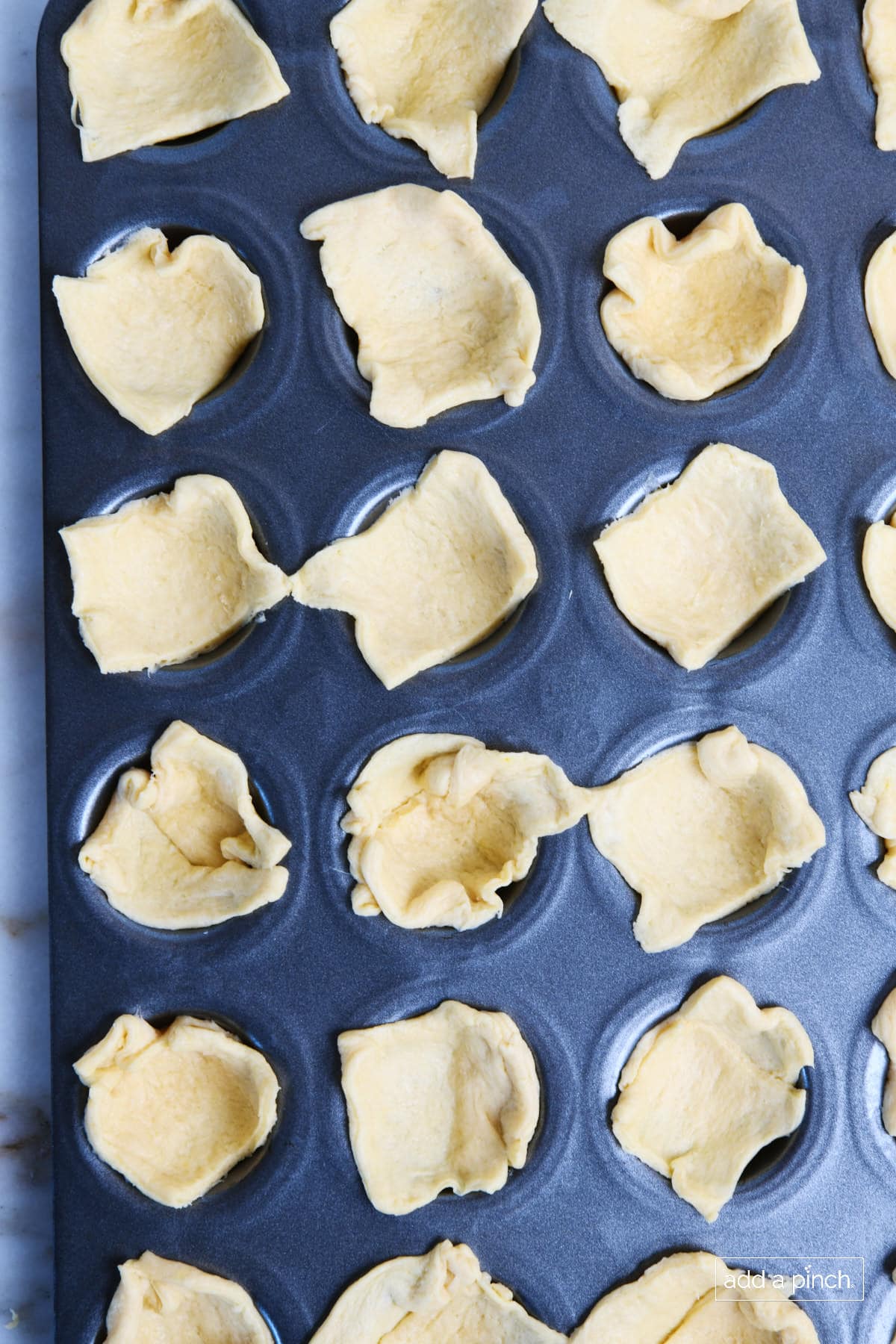 Squares of dough are pressed into the spaces of a mini muffin tin.