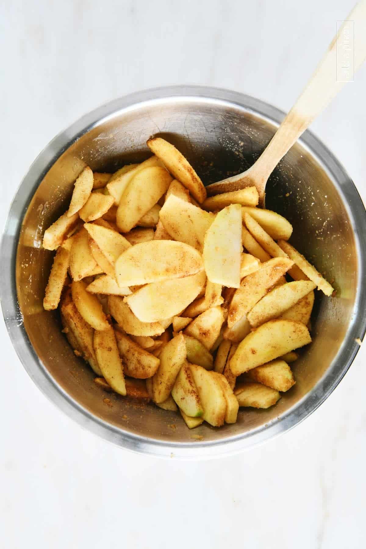 Apple slices are mixed with sugar, vanilla and other ingredients to make apple pie.