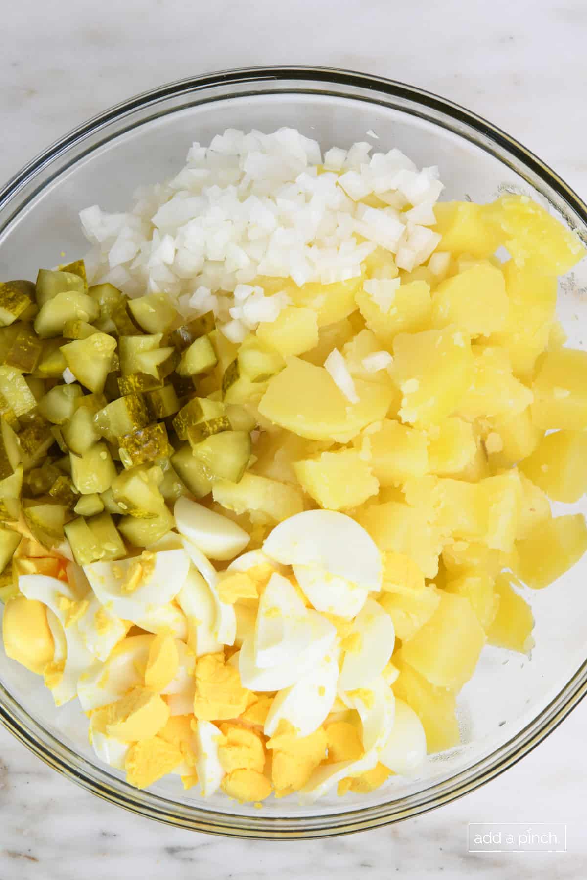 Glass bowl holds the chopped ingredients for Southern potato salad.