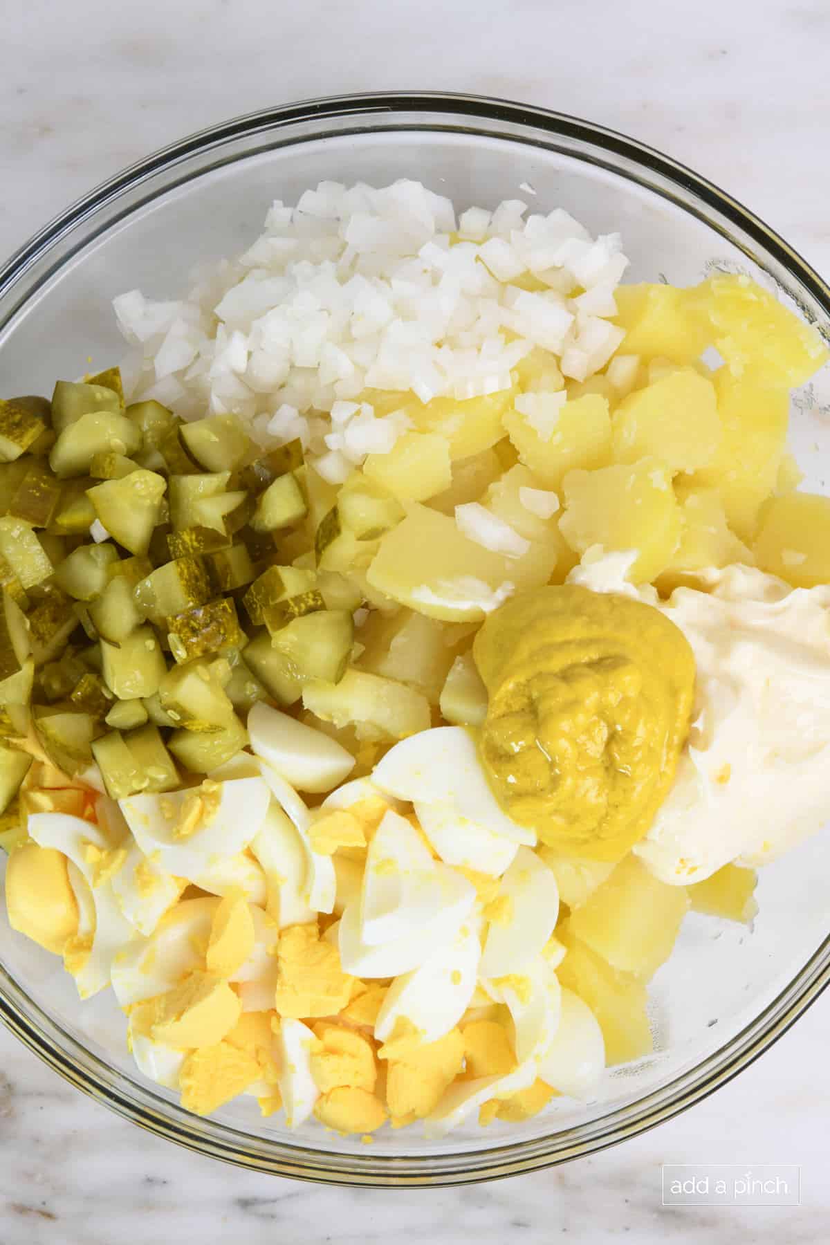 Glass bowl has ingredients for southern potato salad and mustard and mayo added before mixing.