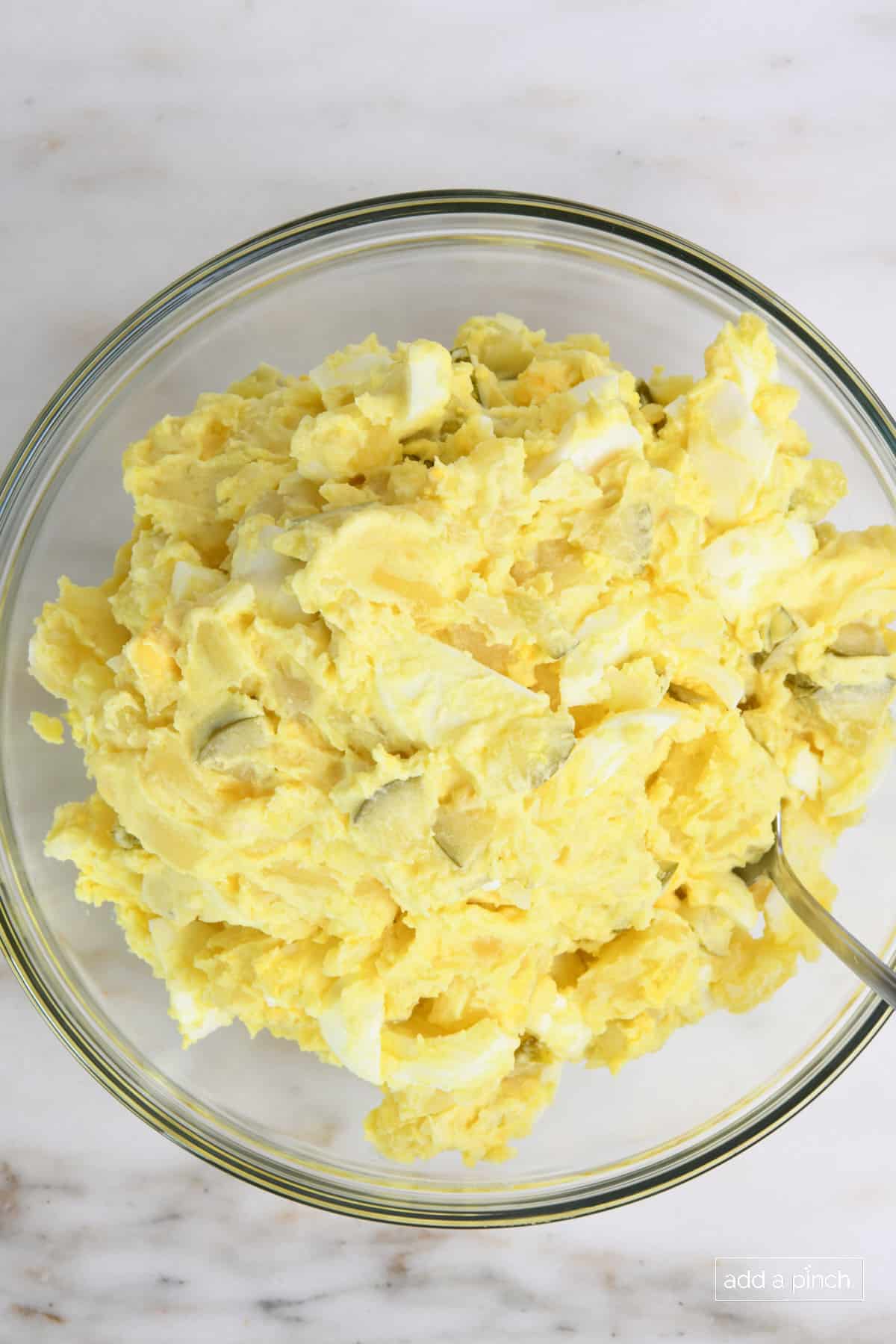 Overhead view of Southern potato salad in a glass bowl with a spoon.
