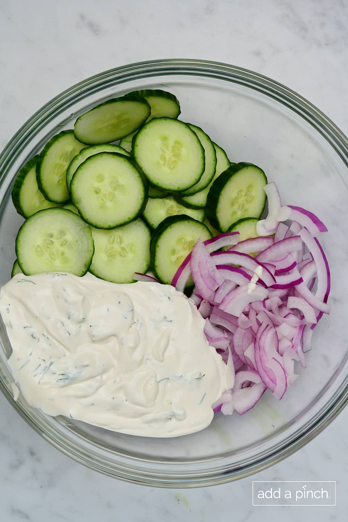 Bowl of slided cucumbers, onions and creamy dressing in a glass bowl.
