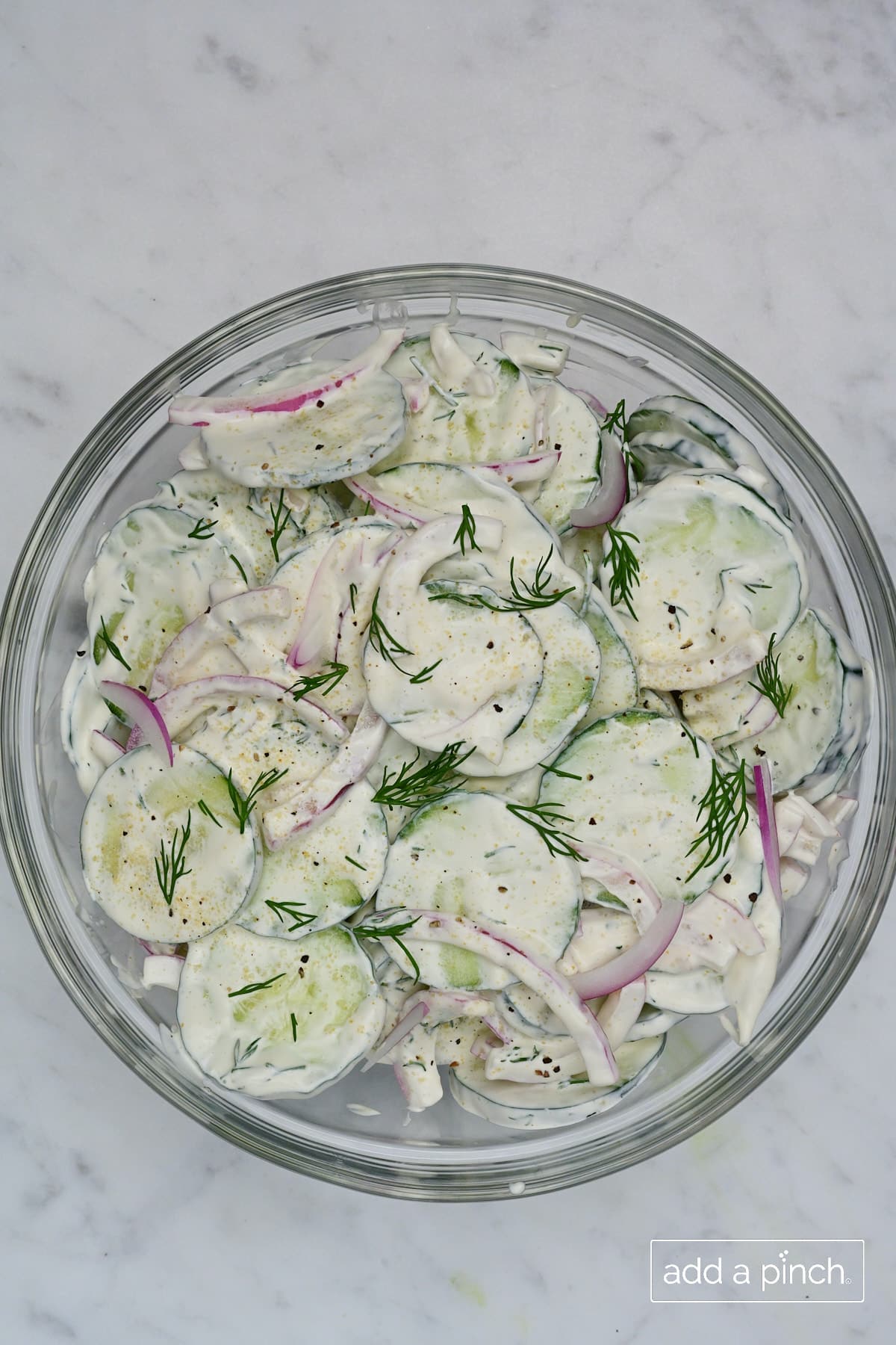 Bowl of creamy cucumber salad with fresh dill on top.