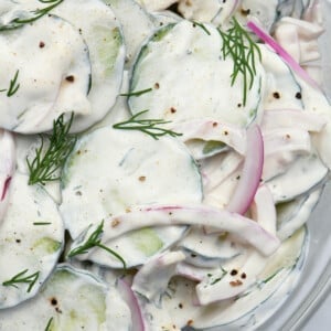 Cucumbers, onions, dill, and creamy dressing for cucumber salad in a glass bowl.