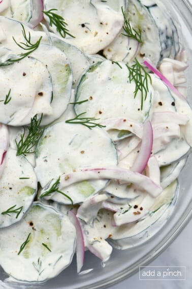 Cucumbers, onions, dill, and creamy dressing for cucumber salad in a glass bowl.