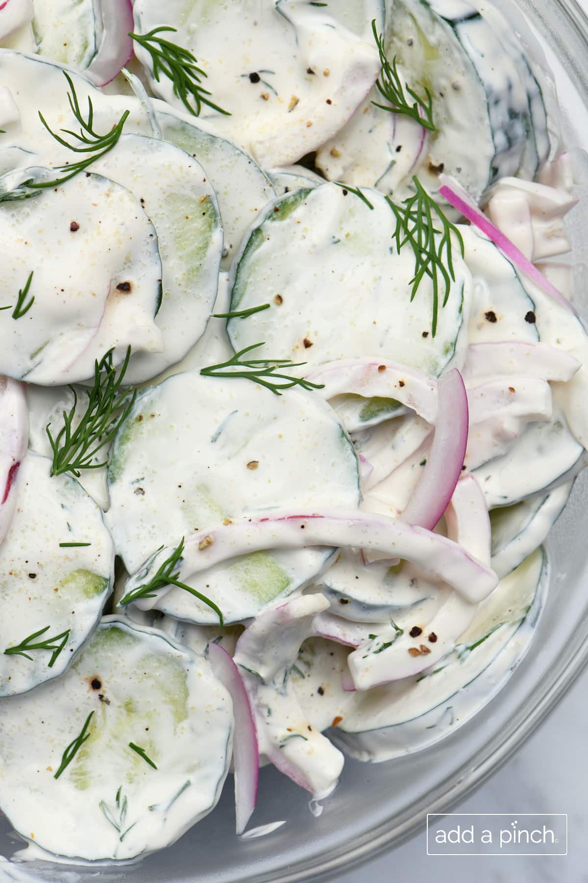 Cucumbers, onions, dill, and creamy dressing for cucumber salad in a glass bowl.