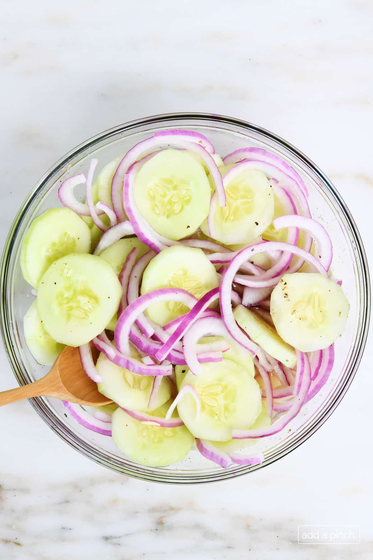 Overhead view of glass bowl with cucumber onion salad. mixed in tangy dressing.  