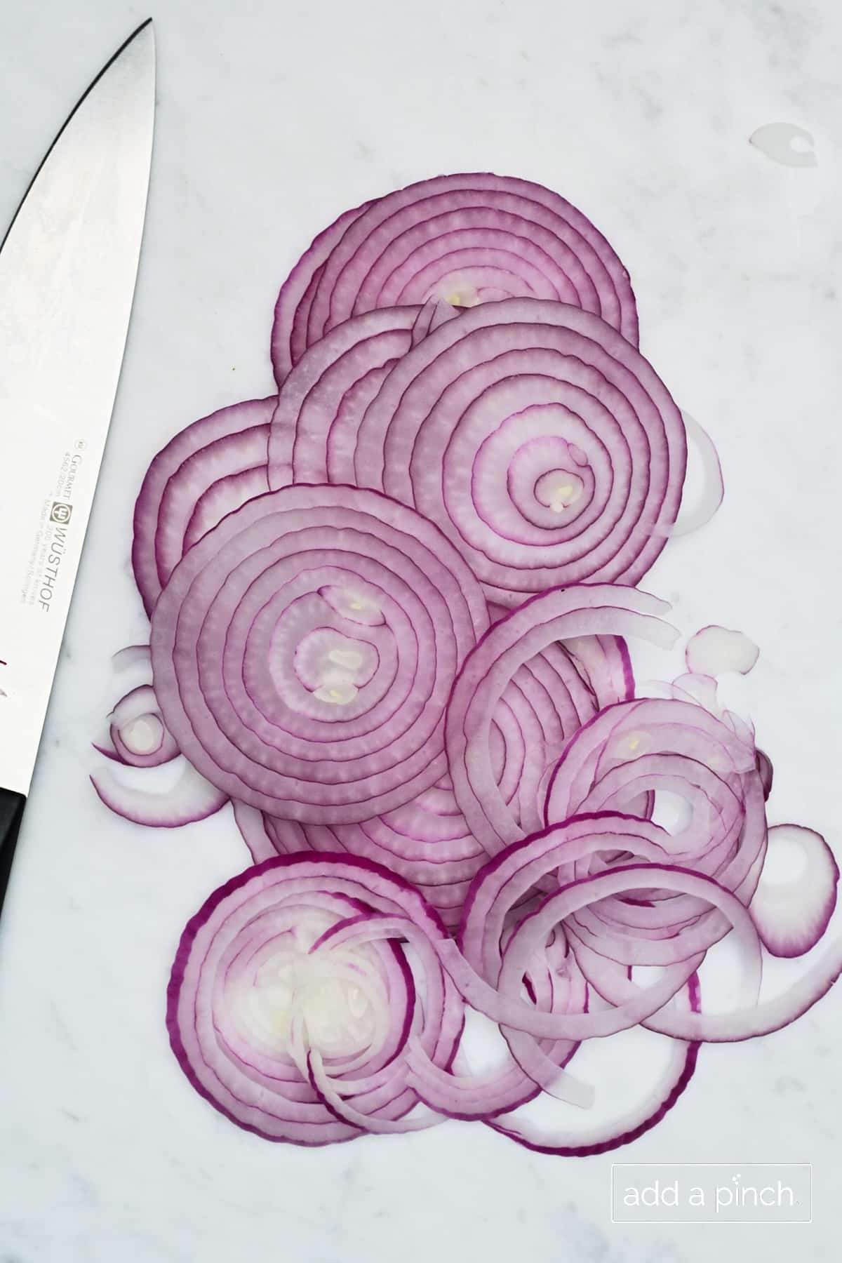 Thinly sliced red onions and a chef's knife on a marble countertop.