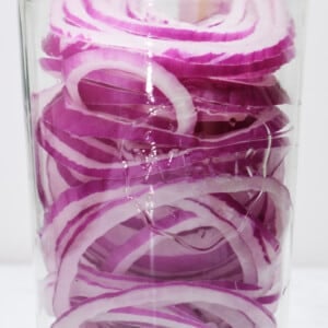Red onion slices in a glass jar.