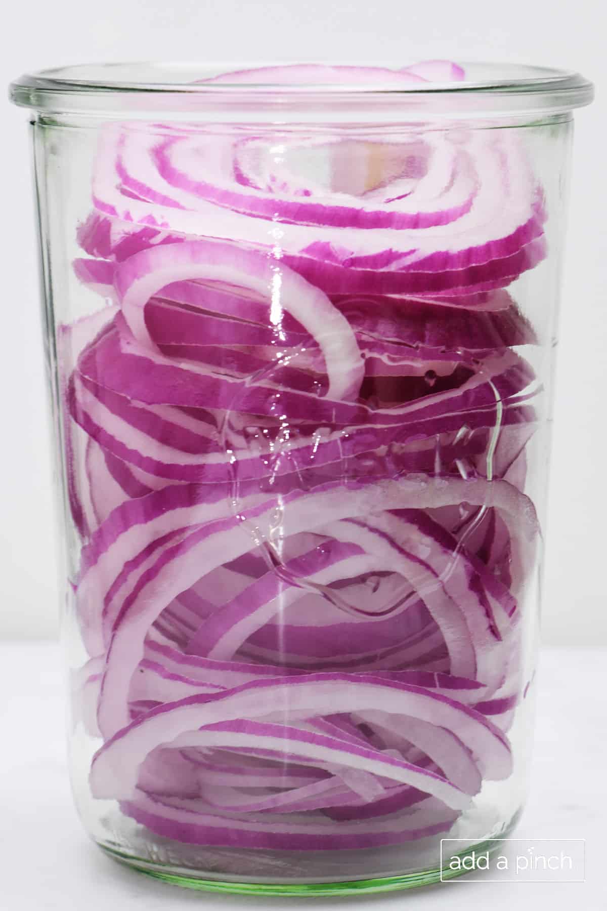 Red onion slices in a glass jar.