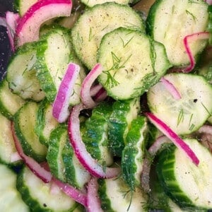Fresh cucumber onion salad in a glass bowl with tangy vinegar dressing and dill garnish.