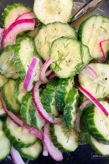 Fresh cucumber onion salad in a glass bowl with tangy vinegar dressing and dill garnish.