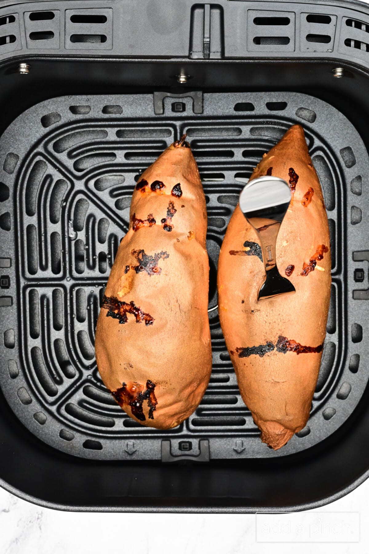 A fork stuck into a sweet potato in air fryer to check for doneness.