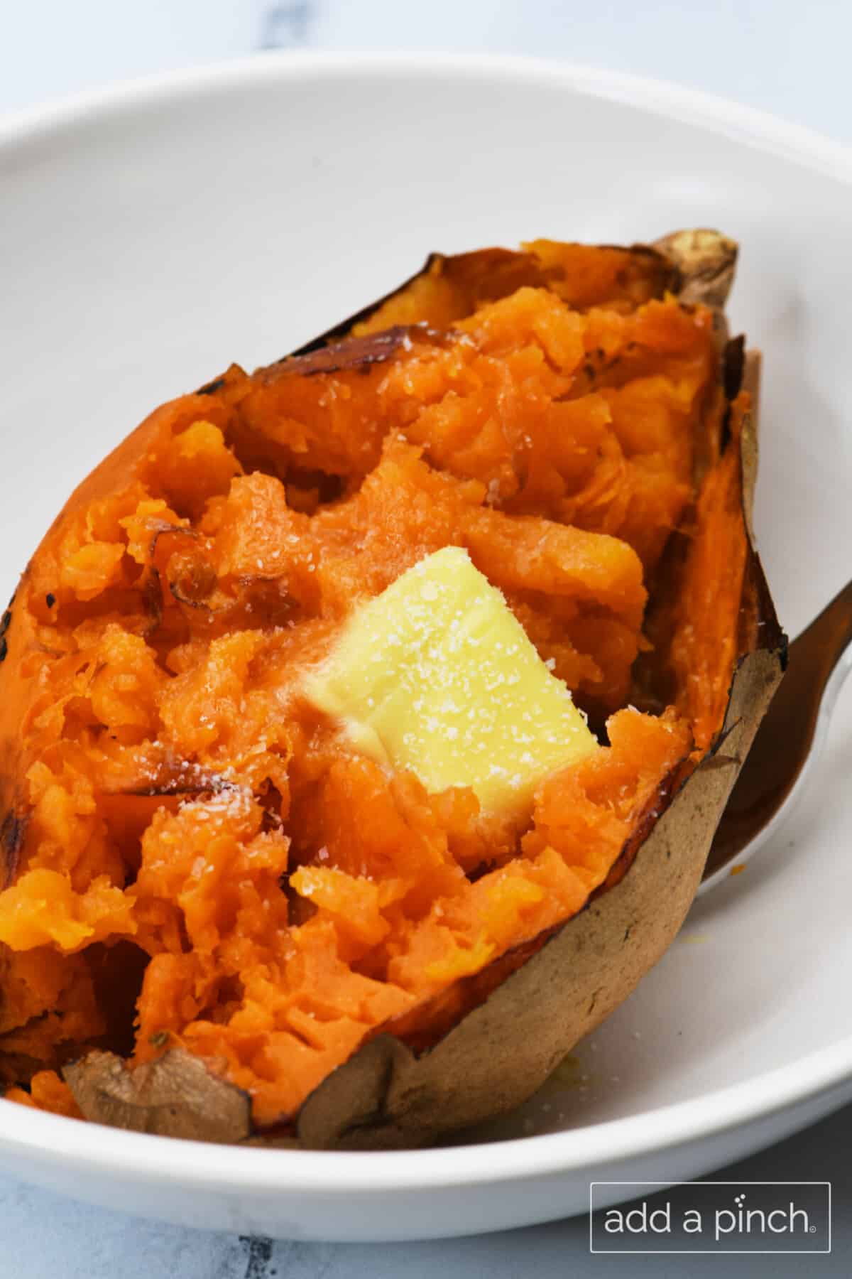 Air fryer baked sweet potato with a pat of butter and sprinkle of salt in a white bowl on marble surface.