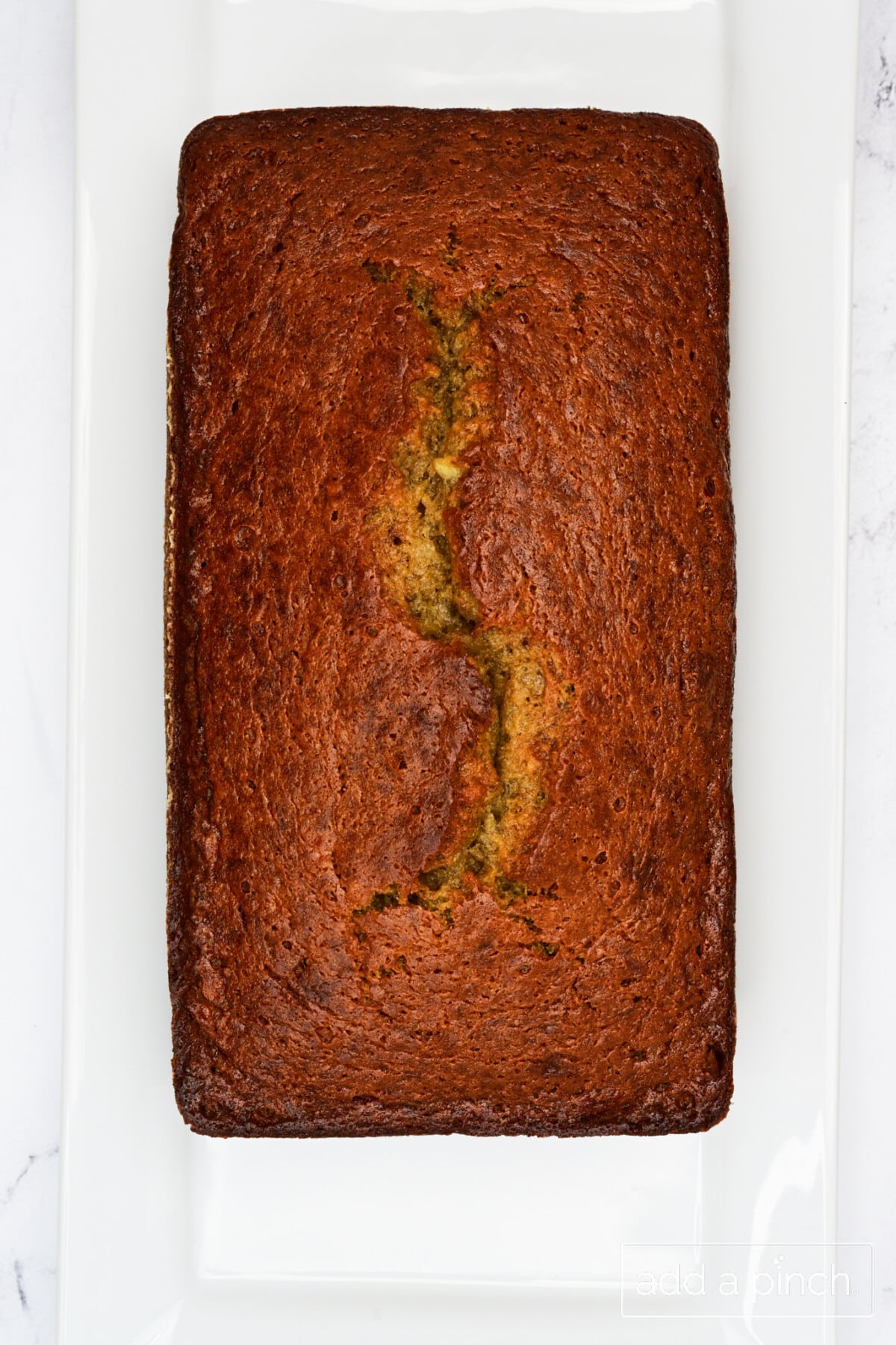 Golden loaf of baked banana bread on a white platter.