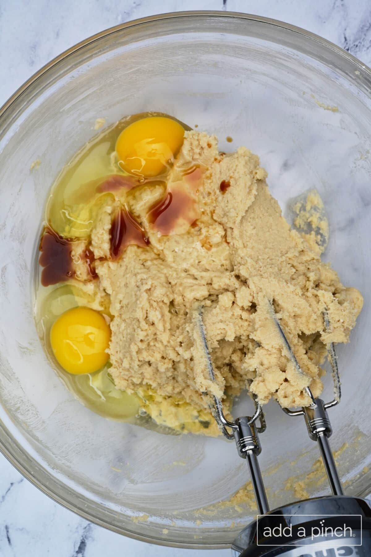 Wet ingredients for chocolate chip cookies are blended together in glass mixing bowl with a hand mixer.