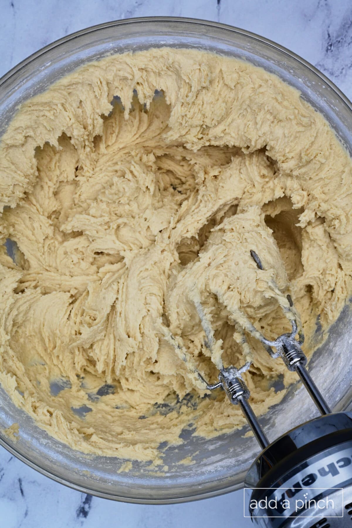 Combined dry and wet ingredients for cookie dough is mixed in a glass mixing bowl.