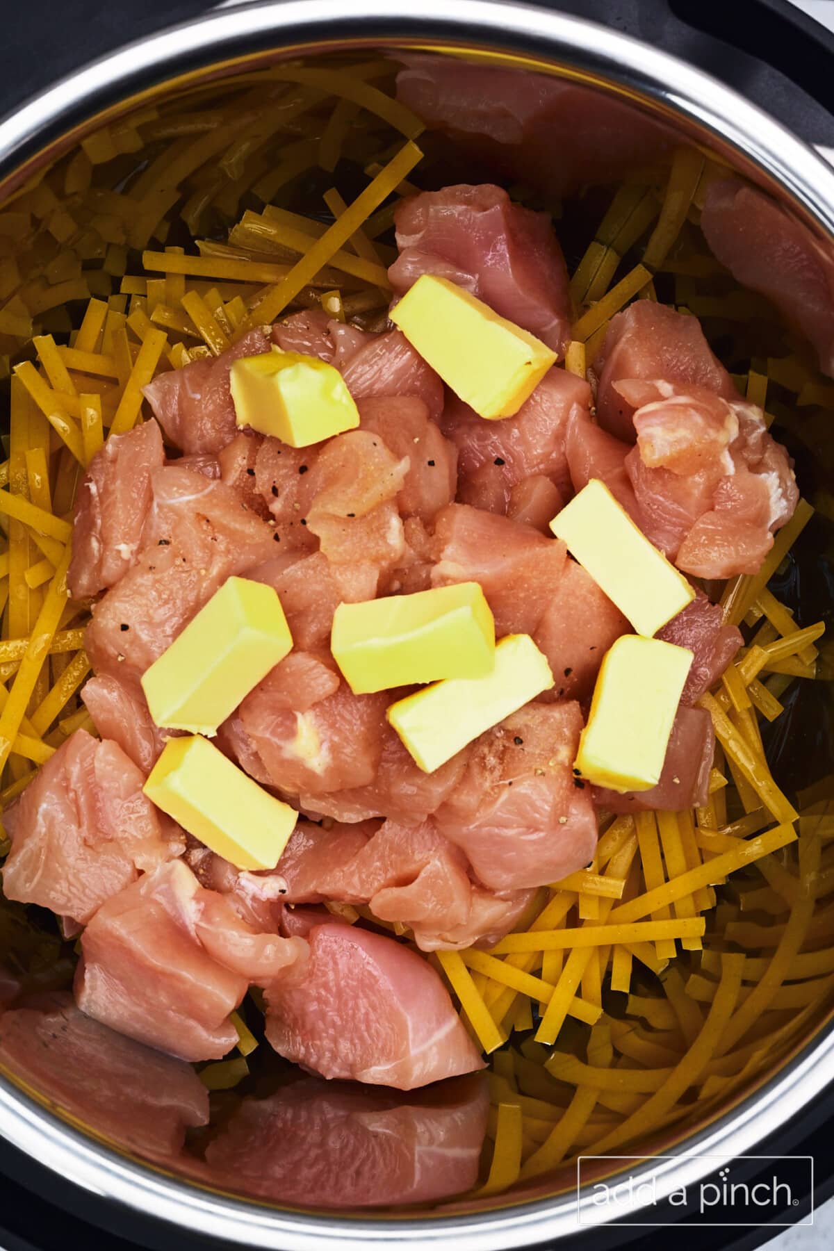 Pasta, chicken, butter, seasonings, and broth in Instant Pot ready to be cooked for chicken Alfredo.