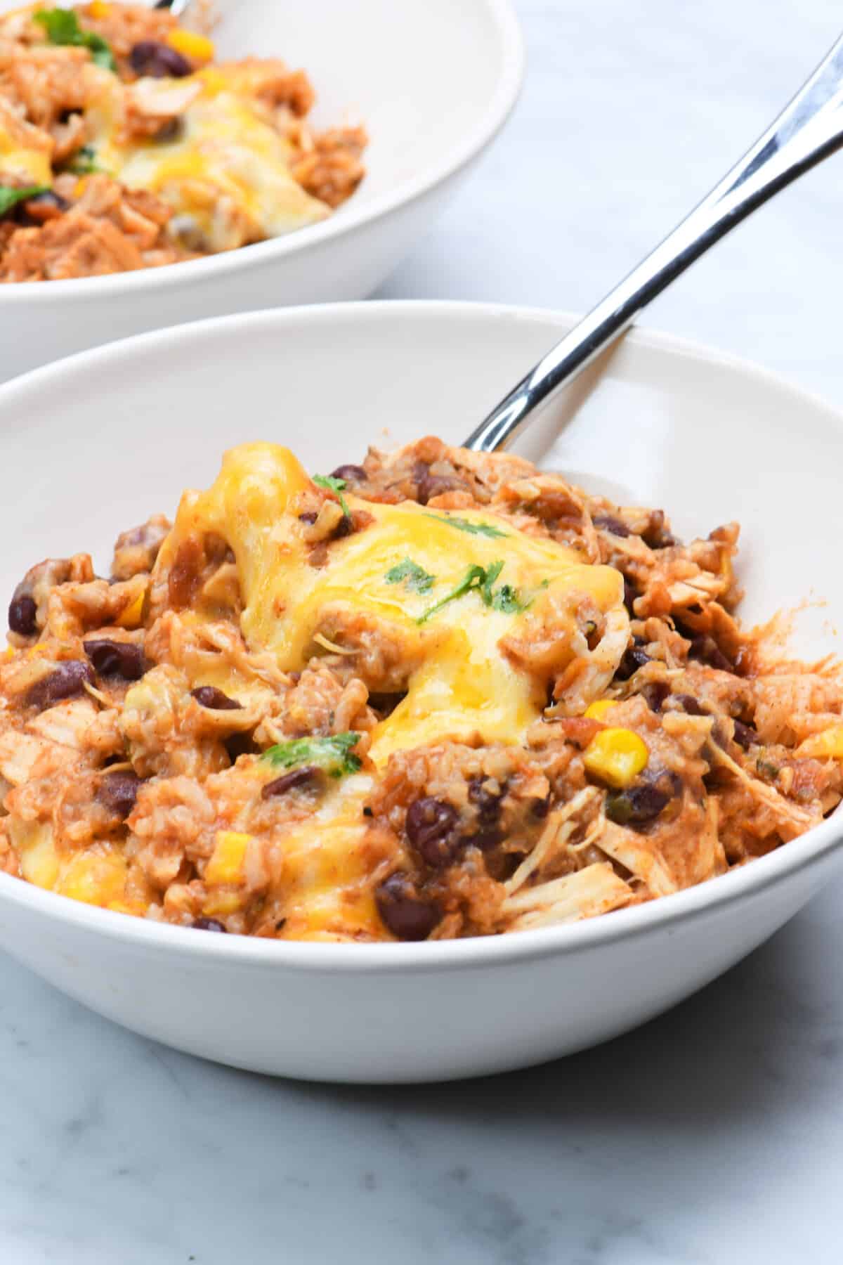 Chicken burrito bowls made with chicken, beans, corn, and rice and topped with cheese and cilantro.