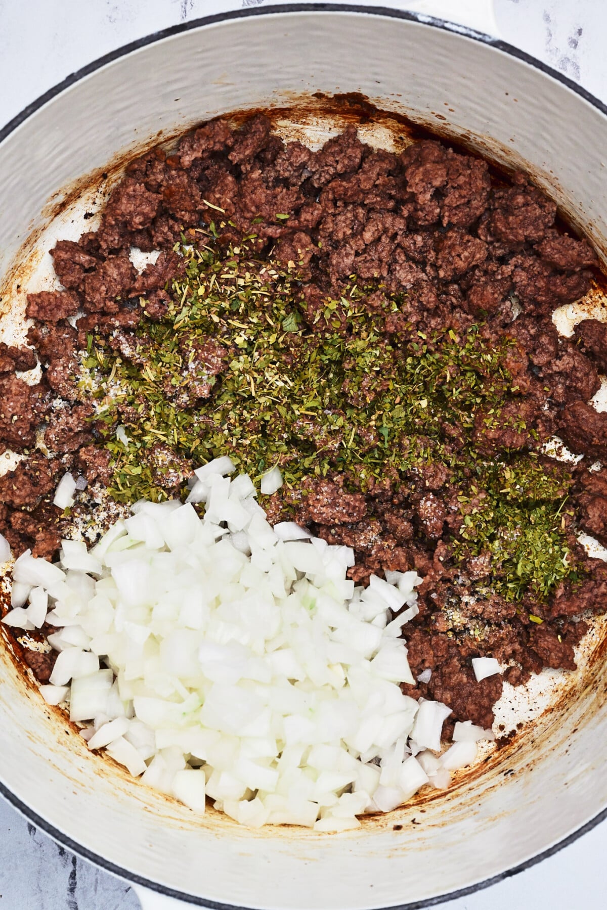 Browned ground beef with onion and seasoning in a white Dutch oven.