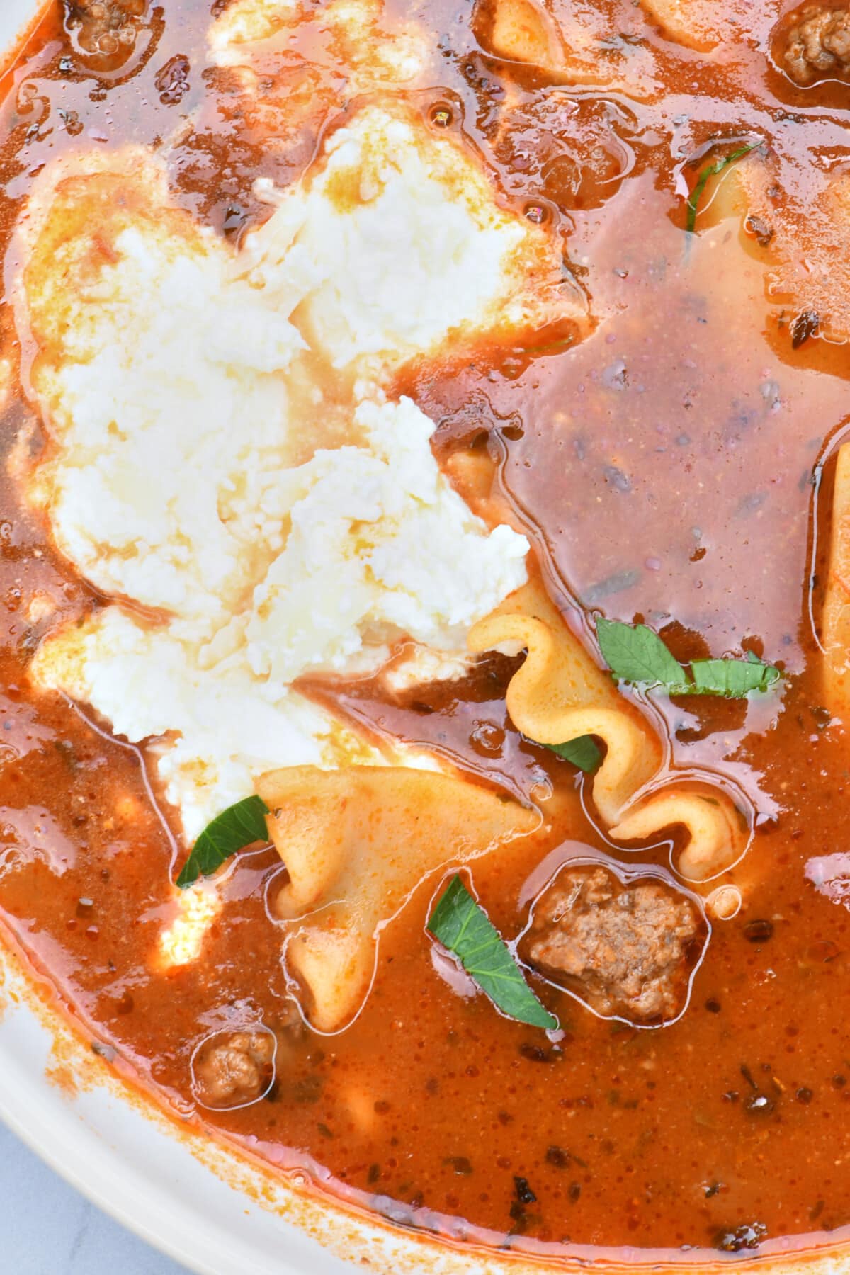Bowl of Lasagna Soup topped with creamy three cheese topping and fresh green herbs.