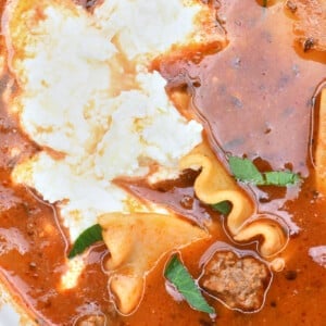 Bowl of Lasagna Soup topped with creamy three cheese topping and fresh green herbs.