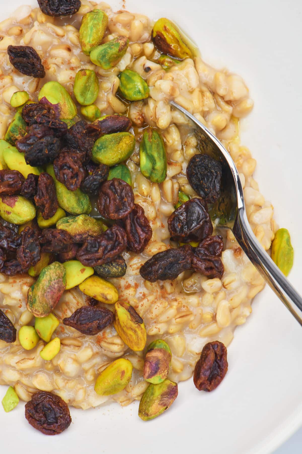 Cooked oat groats in white bowl topped with pistachios and raisins.