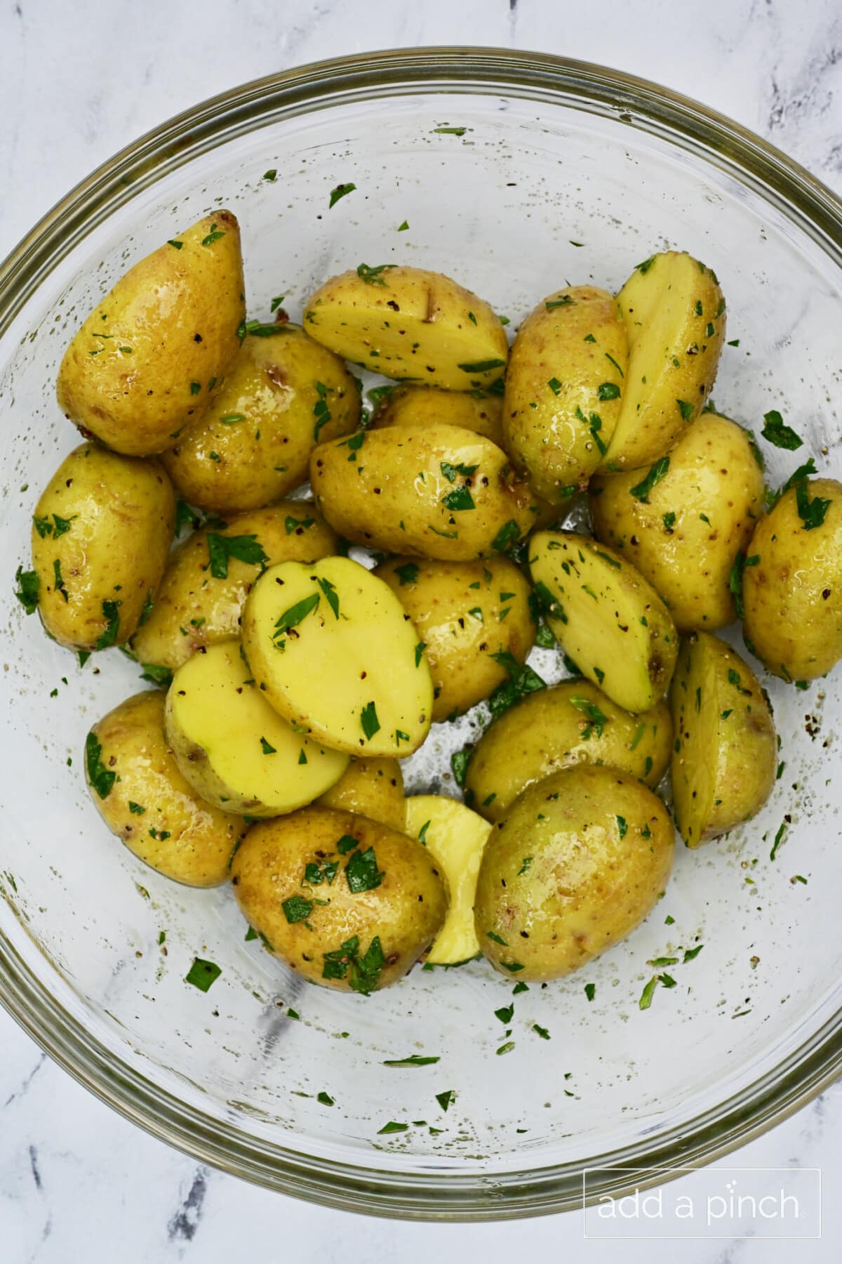 Halved baby potatoes seasoned in a glass mixing bowl.