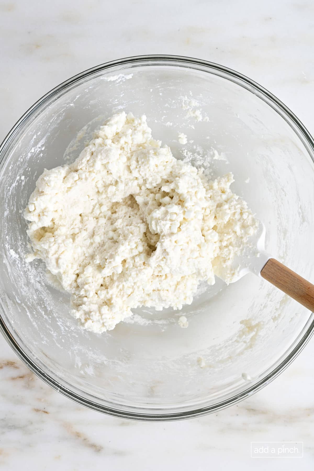 Homemade two ingredient pizza dough in a glass bowl with a spatula.