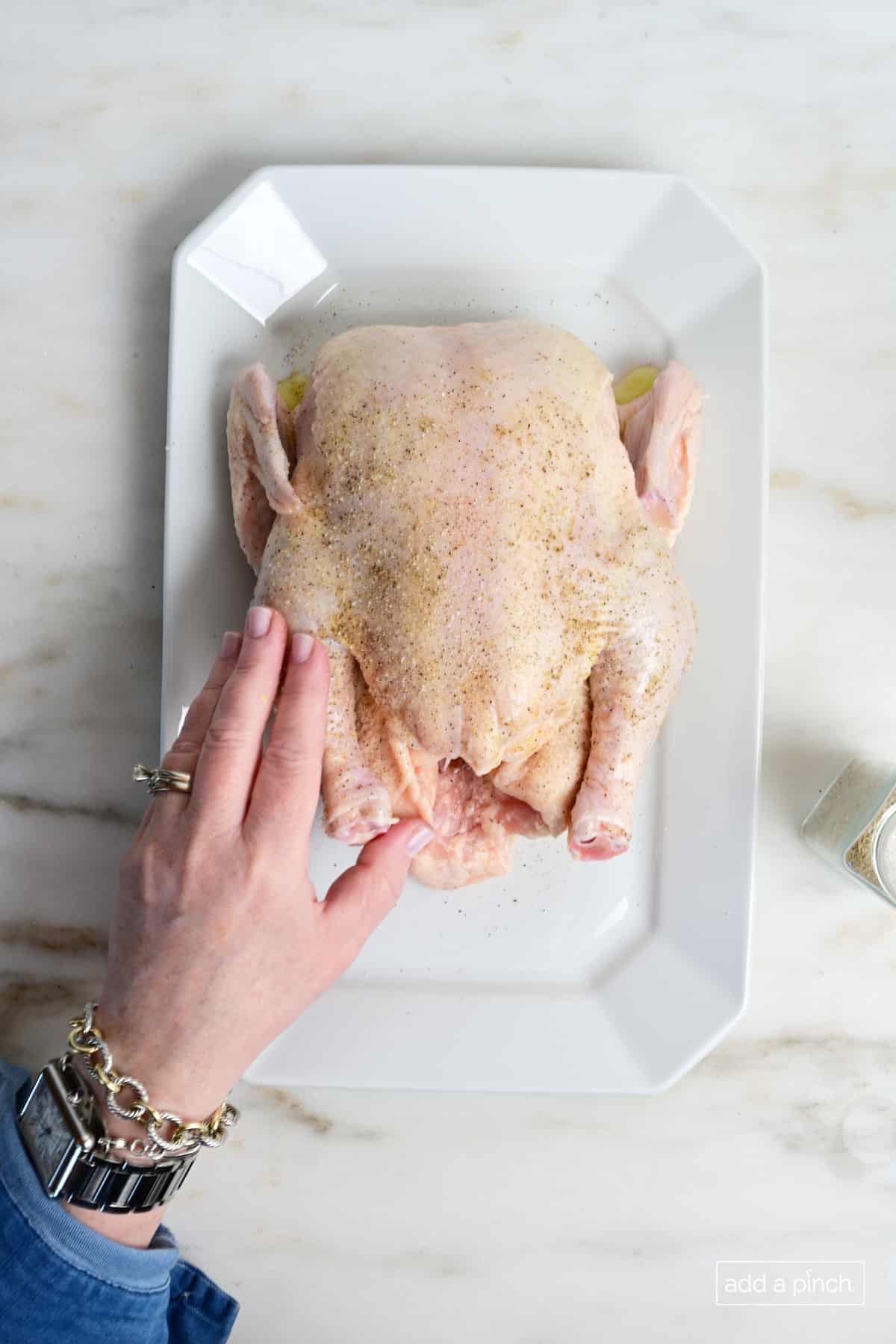 Chicken coated with olive oil and rubbed with Stone House Seasoning on a white platter.