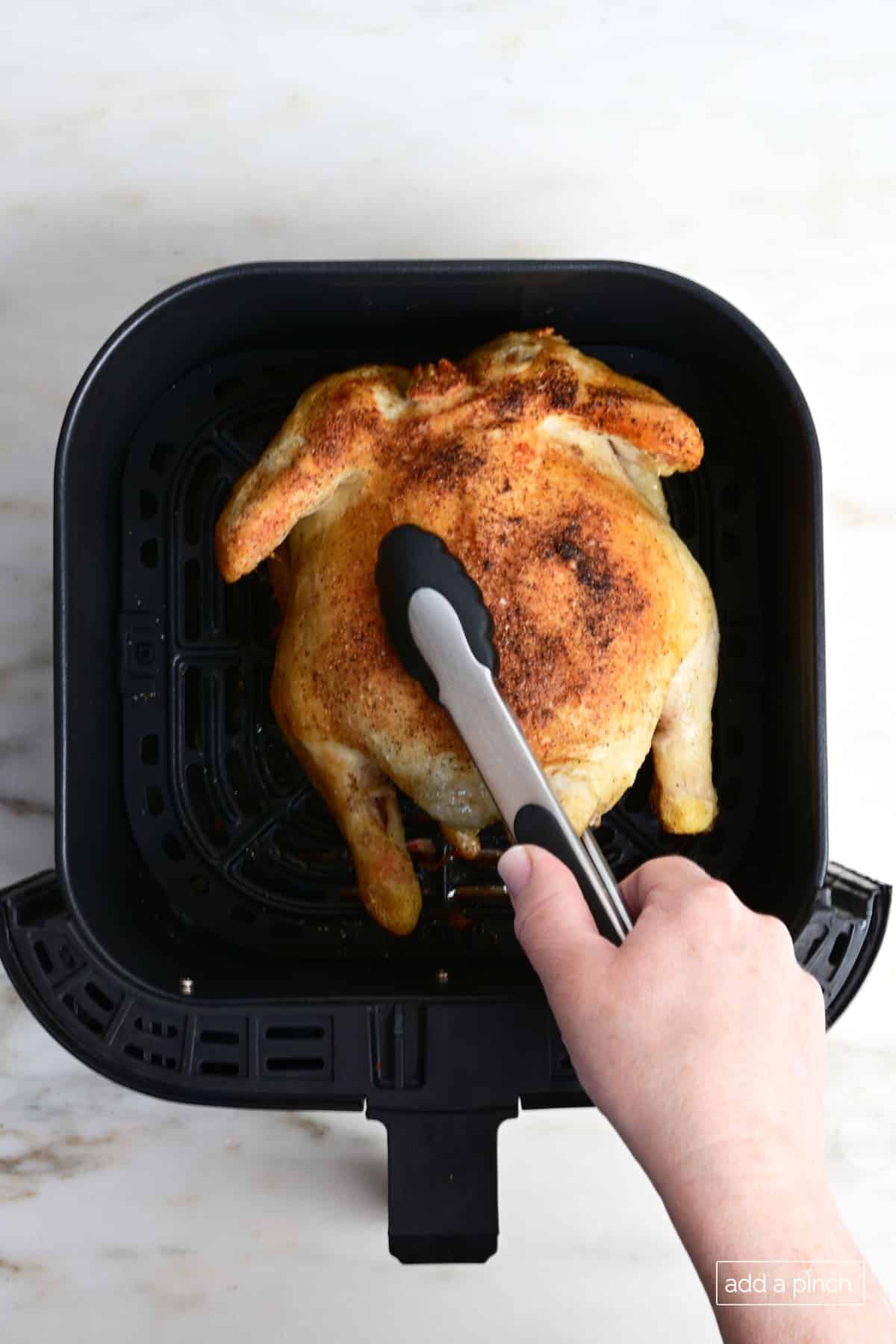 Whole chicken in air fryer being turned with tongs.