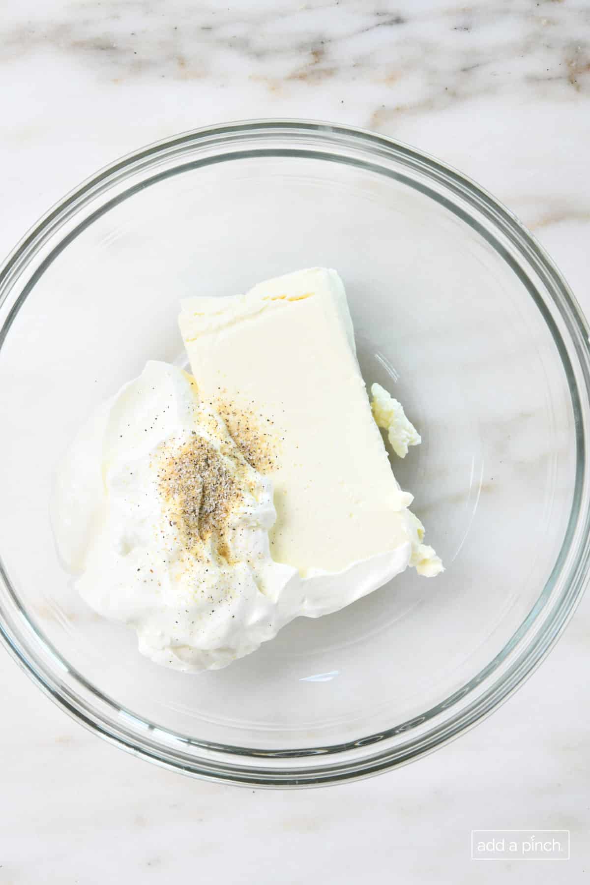 Cream cheese, sour cream, and Stone House Seasoning in a glass mixing bowl.