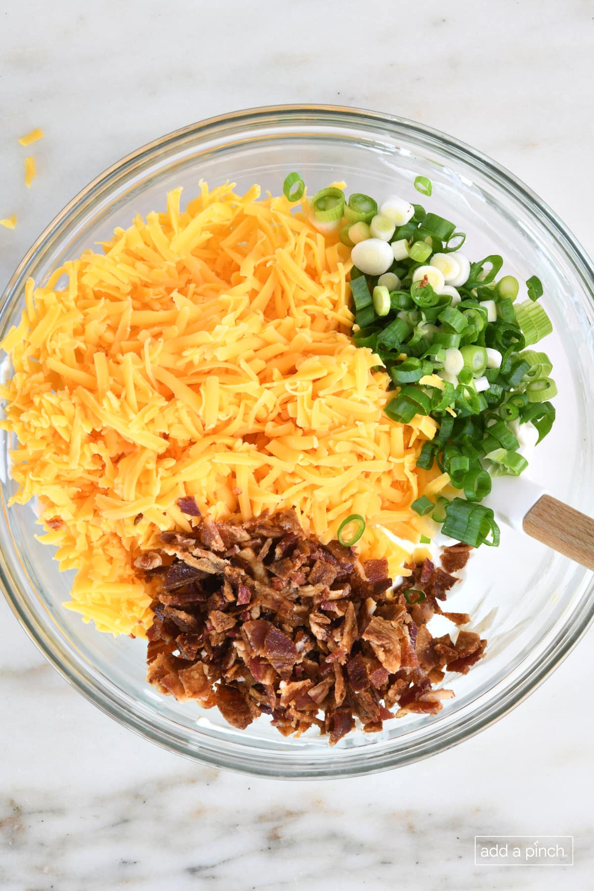 Bacon cheddar dip in a mixing bowl with crumbled bacon, shredded cheese, and sliced green onions.