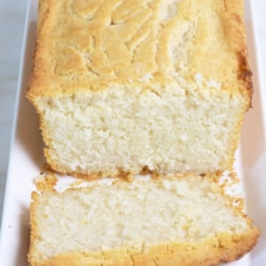 Golden beer bread on a white platter with a slice cut.