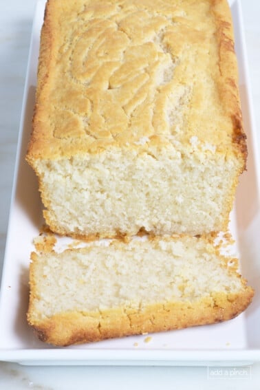 Golden beer bread on a white platter with a slice cut.