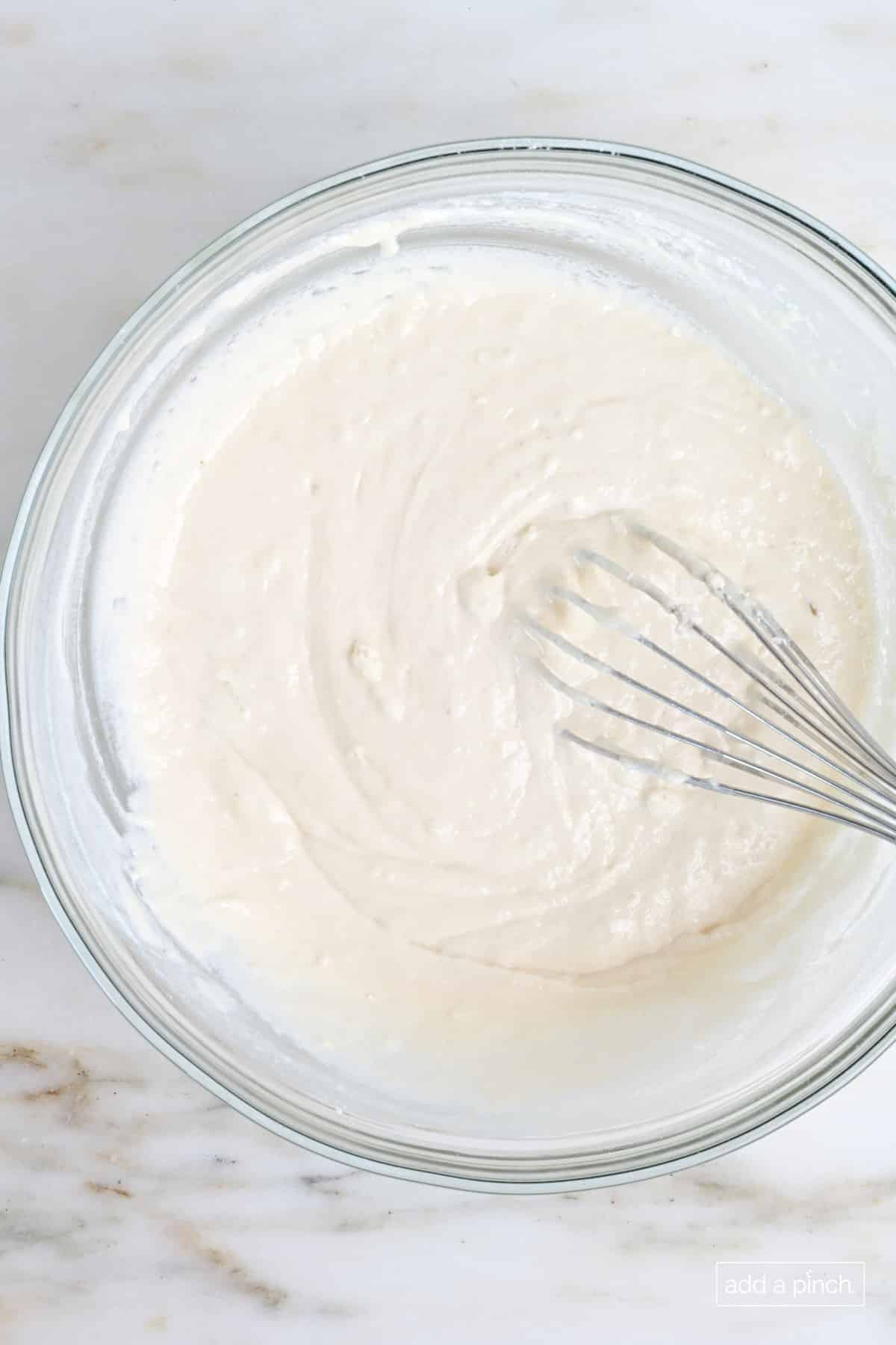 Beer bread batter in a glass mixing bowl with a whisk.