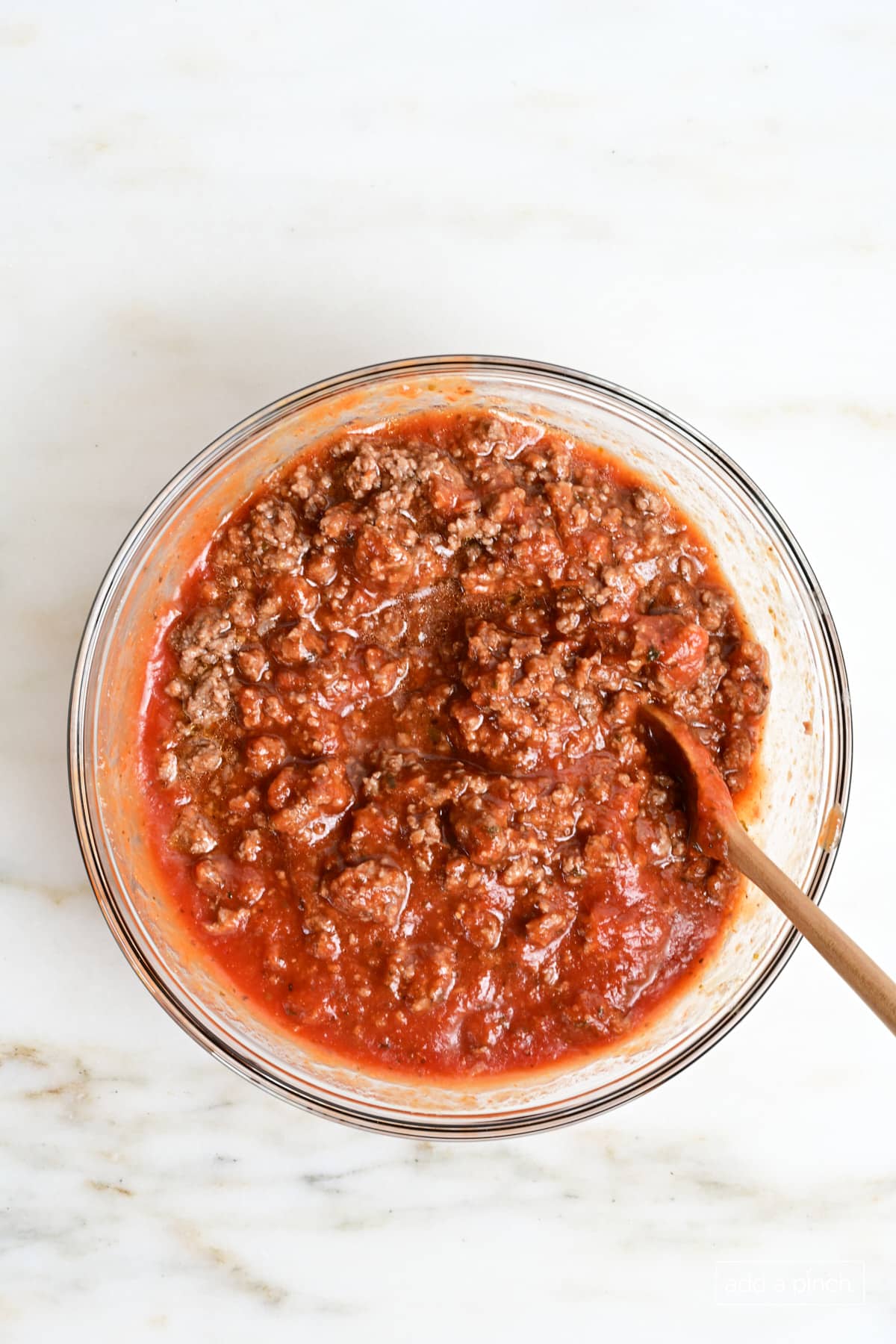 Marinara Sauce in a glass mixing bowl with a wooden spoon.