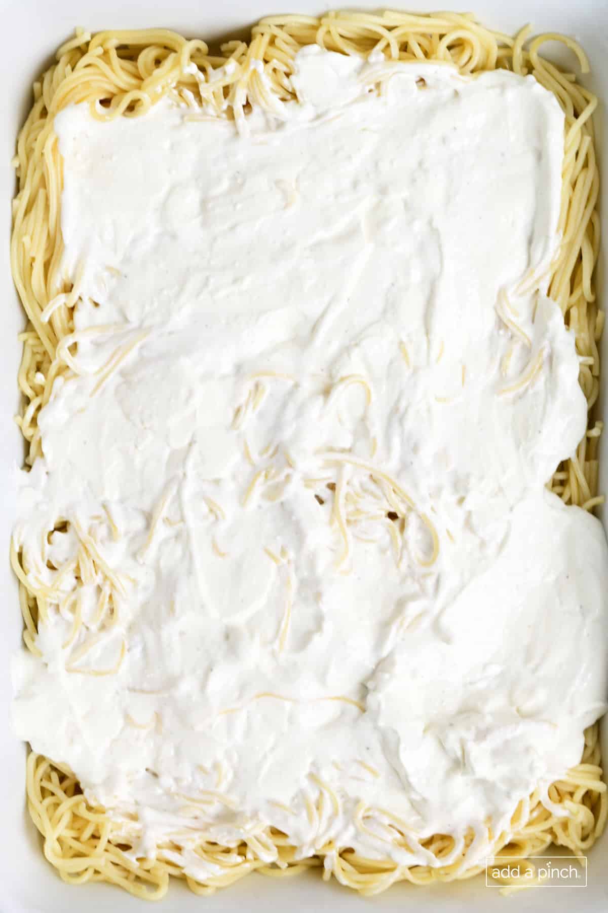Cooked spaghetti and cheese layer in a baking dish.