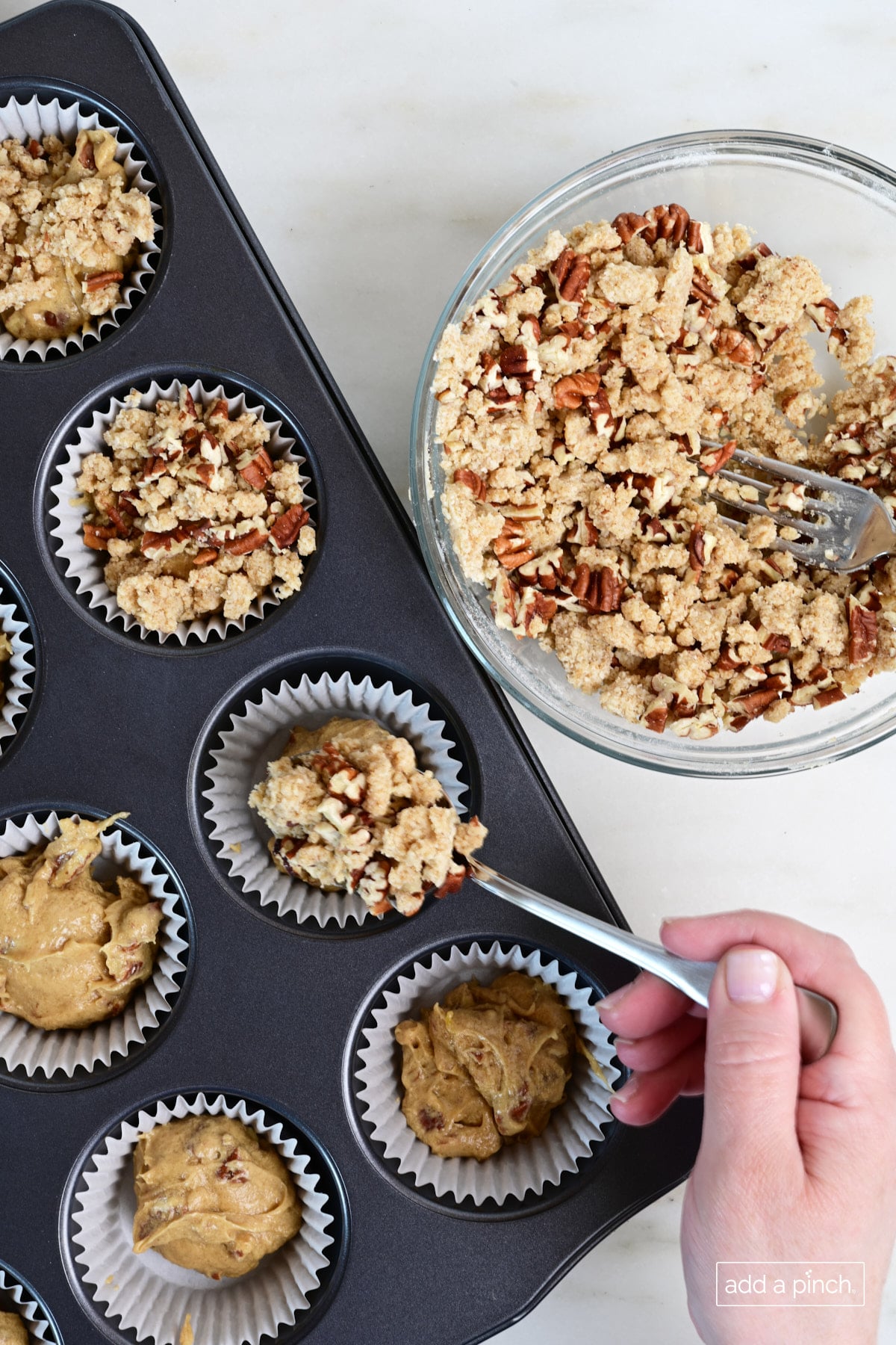Streusel topping being spooned onto pecan pie muffins.