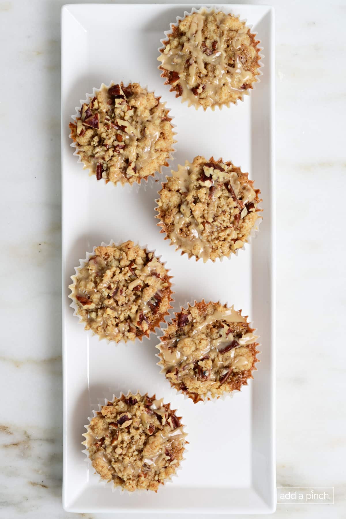 Pecan pie muffins with streusel topping and maple glaze on a white platter.