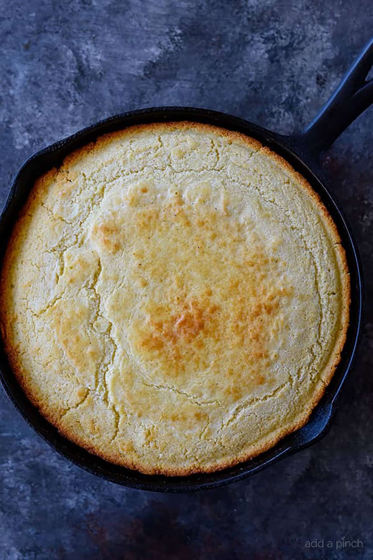 Overhead view of cornbread with crisp edges in a cast iron skillet.