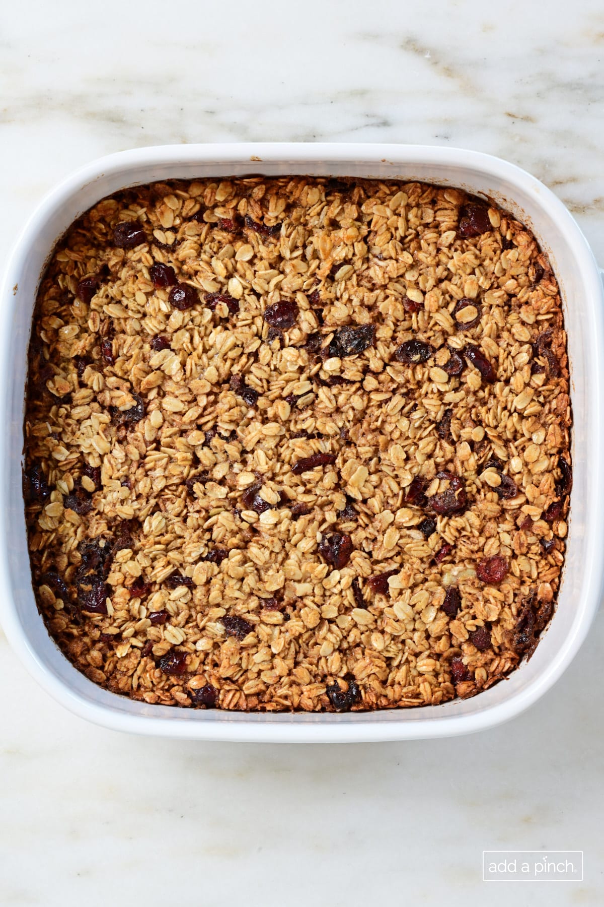 Baked oatmeal in a white baking dish on a marble surface.