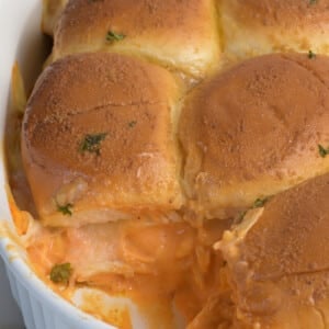 Buffalo chicken sliders in a baking dish topped with a buttery spread.